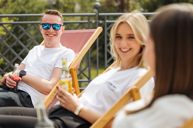 Zwei Kollegen sitzen lachend im Liegestuhl und haben ein Getränk in der Hand