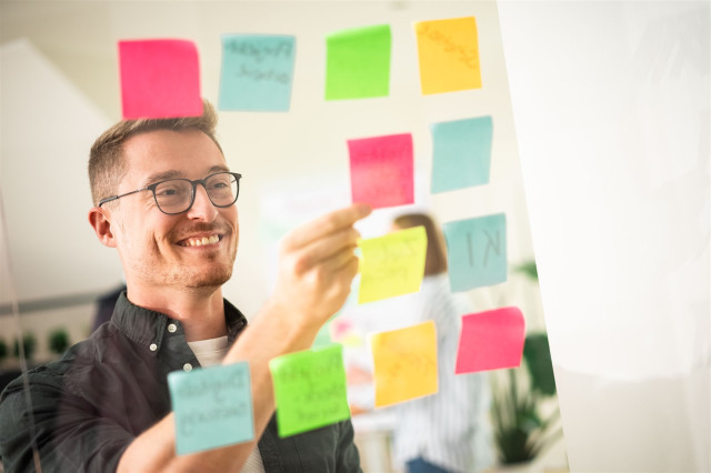 Mitrabeiter klebt bunte Post-Its an durchsitiges Board