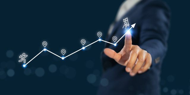 Eine Hand zeigt auf einen gemalten Berg mit verschiedenen Zielpunkten. Ein Strichmännchen läuft diesen Berg hoch